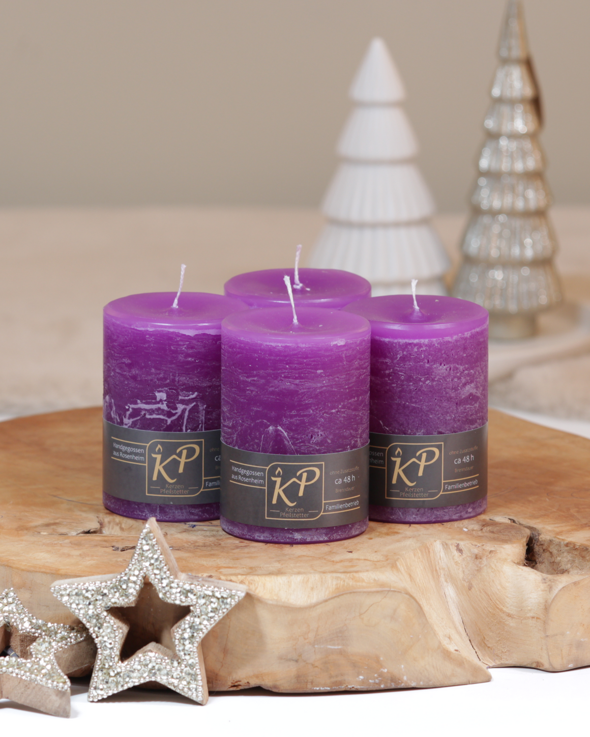 Vier Tischkerzen in lila dekorativ auf einem Holztisch mit Weihnachtsdeko im Hintergrund.