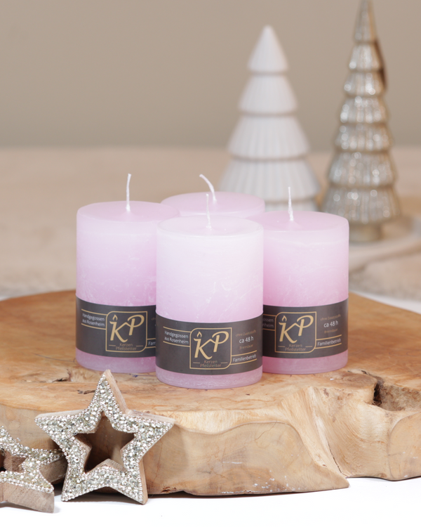 Vier Tischkerzen in pastellrosa dekorativ auf einem Holztisch mit Weihnachtsdeko im Hintergrund.