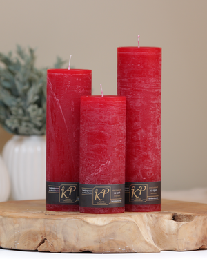 Blütenkerzen in weihnachtsrot in drei Größen – dekorativ auf einem Holztisch mit Pflanze im Hintergrund.