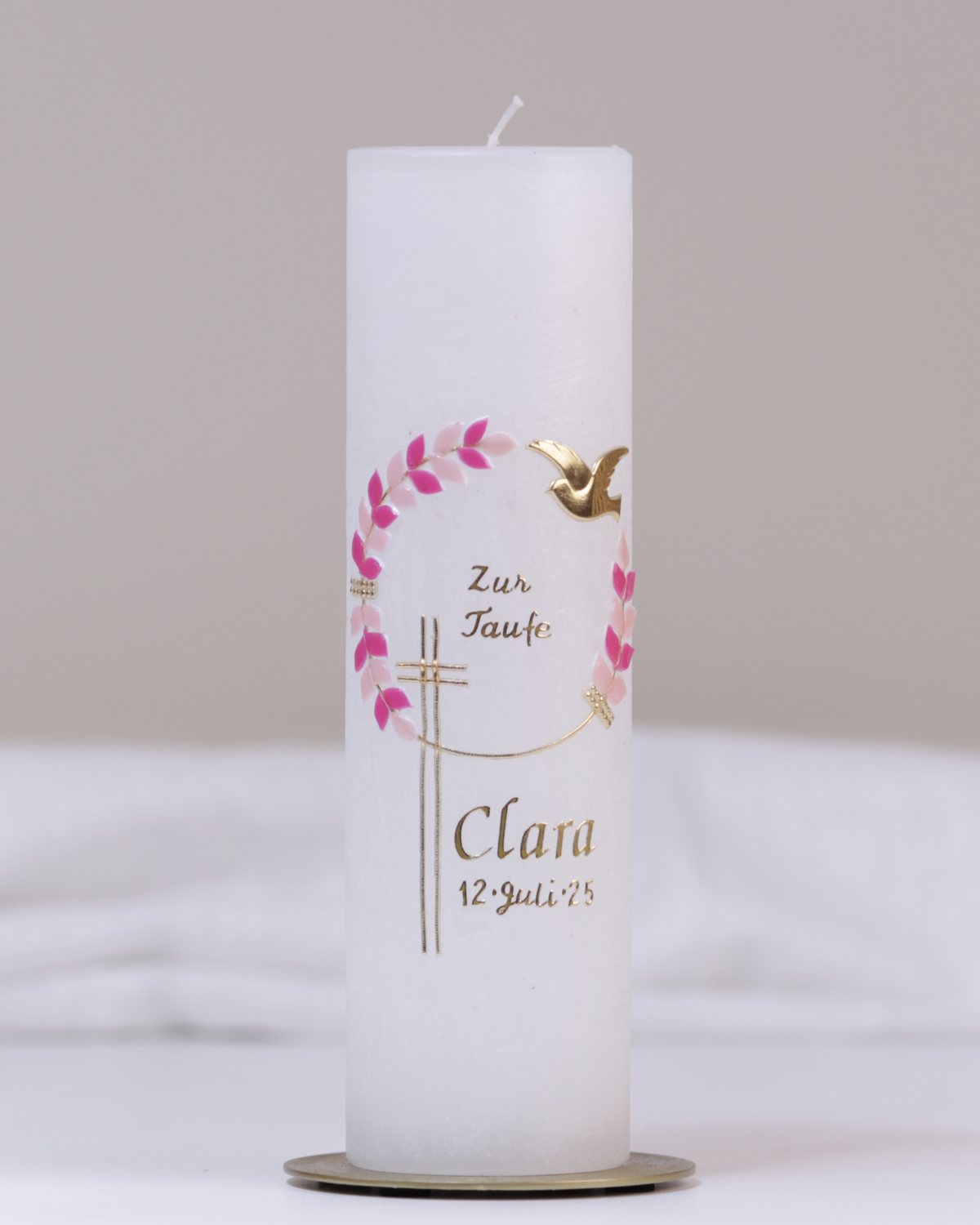 Weiße Taufkerze mit gold-pinker Verzierung aus Kreuz, Blumenranke, Taube und „Zur Taufe“-Schriftzug.