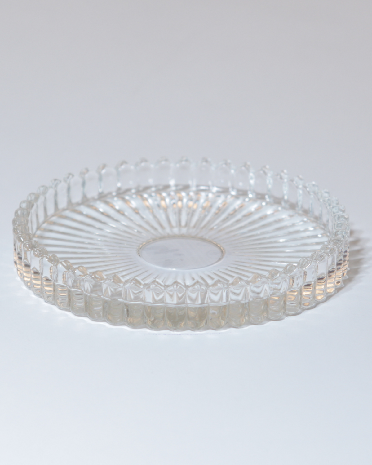 Kerzenteller aus klarem Glas mit facettierter Struktur.